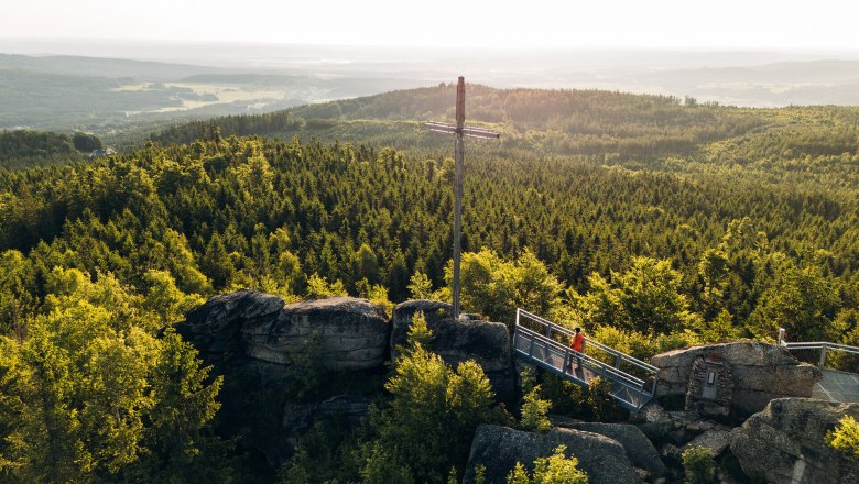 Nebelstein Ausblick, Landschaft, Kreuz, Thayatalweg 630, Zusatzetappe Weg entlang der Lainsitz, © Waldviertel Tourismus, Melanie Többe Aussichtsplattform auf einer Felsformation mit Blick über dicht bewaldete Hügel im Waldviertel, unter einem klaren blauen Himmel.