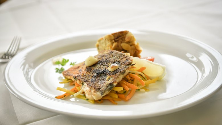 Xunder Genuss, © Moorheilbad Harbach Ein Teller mit gebratenem Fischfilet auf Gemüsestreifen und einer Beilage auf weißem Tischtuch.