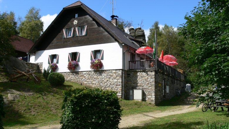 Nebelsteinhütte, © Waldviertel Tourismus Eine Berghütte mit Blumen und Sonnenschirmen auf einer Terrasse.