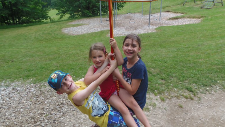 Seilbahn, © Marktgemeinde Bad Großpertholz Drei Kinder schaukeln fröhlich an einer Seilbahn auf einem Spielplatz.