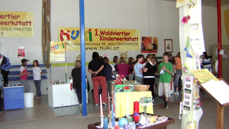 Huki, © HUKI Innenansicht einer Kinderwerkstatt mit Menschen und Bastelmaterialien.