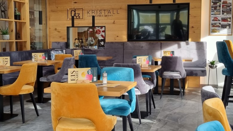 Sonnengarten im Café Kristall, © Café Pension Kristall Innenansicht eines modernen Cafés mit bunten Samtstühlen und Holzwänden.