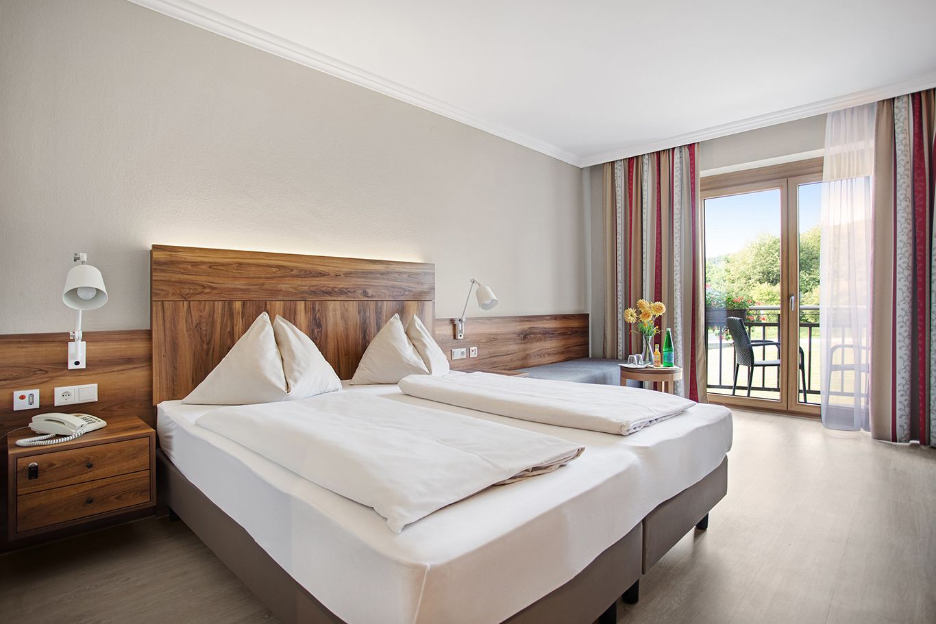 Ein gemütliches Hotelzimmer mit Doppelbett, Holzmöbeln und Balkon mit Blick ins Grüne.