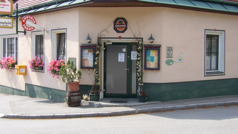Eingang eines traditionellen Gasthauses mit Blumen und Schildern.