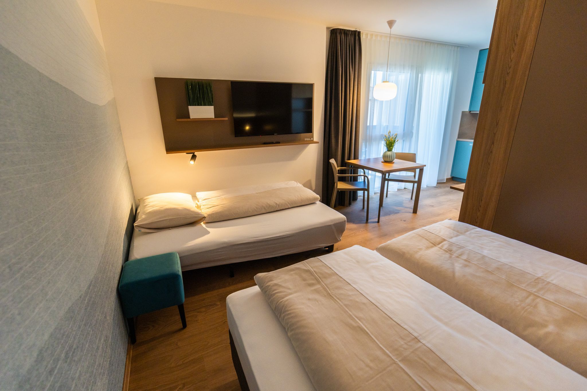 Modern eingerichtetes Hotelzimmer mit zwei Betten, einem Tisch und einem Fernseher an der Wand.