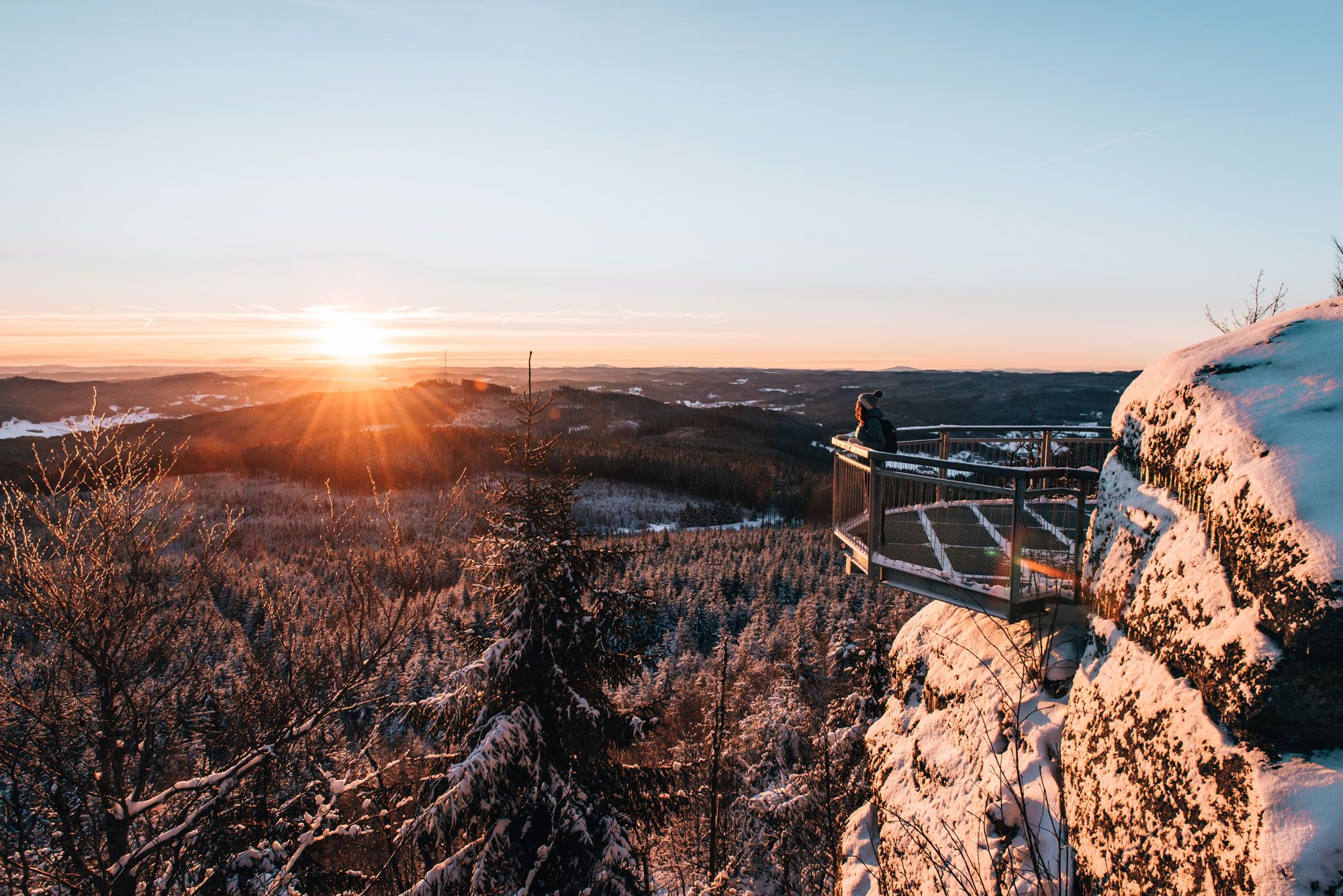 Person auf einer Aussichtsplattform im verschneiten Waldviertel bei Sonnenuntergang.