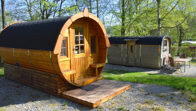 Zwei h&ouml;lzerne Fassh&uuml;tten in einem gr&uuml;nen Park mit B&auml;umen.