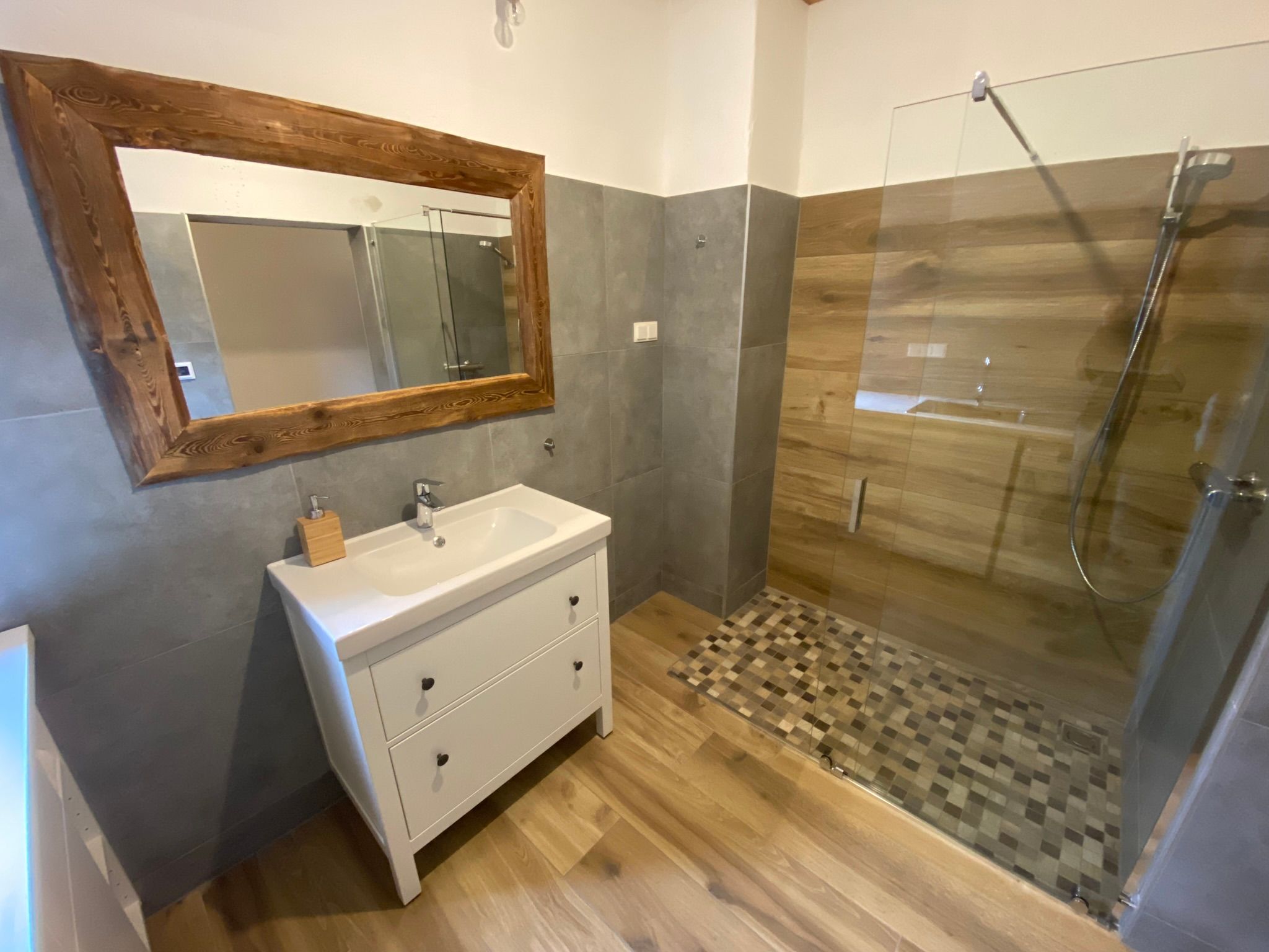 Modernes Badezimmer mit Holz- und Glaselementen, einem großen Spiegel und einer begehbaren Dusche.