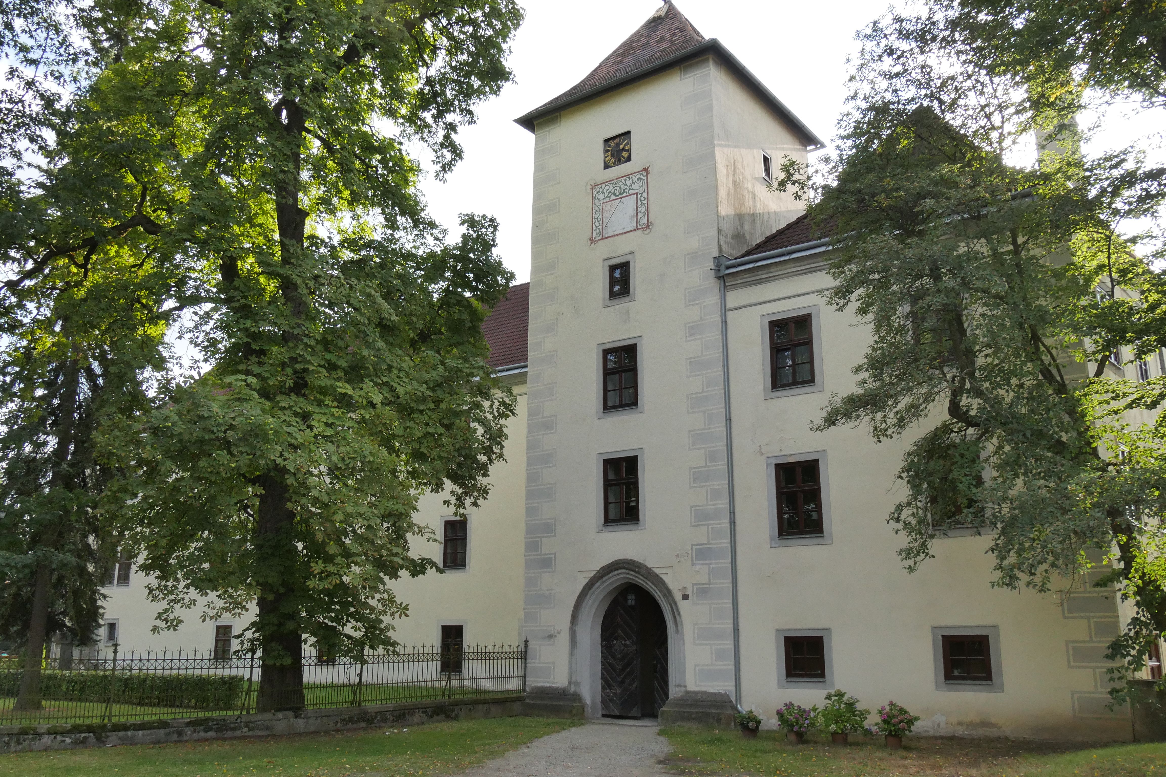 Historisches Gebäude mit Turm und Bäumen im Vordergrund.