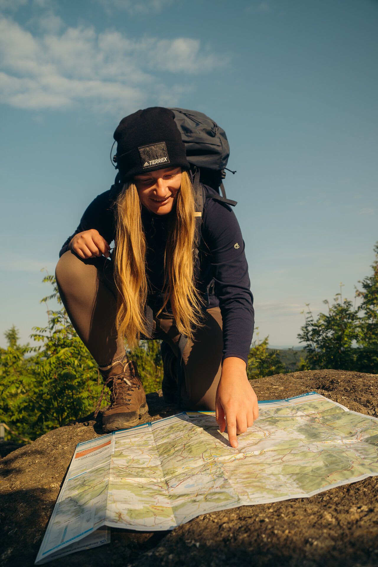 Eine Frau in Wanderoutfit zeigt auf einen Punkt auf einer Wanderkarte, die auf einem Felsen liegt