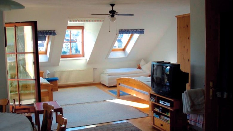 Innenansicht eines gem&uuml;tlichen Dachgeschosszimmers mit Holzm&ouml;beln, zwei Betten, einem Fernseher und Dachfenstern.