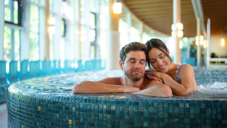 Ein Paar entspannt sich in einem Whirlpool in einem modernen Spa mit gro&szlig;en Fenstern.