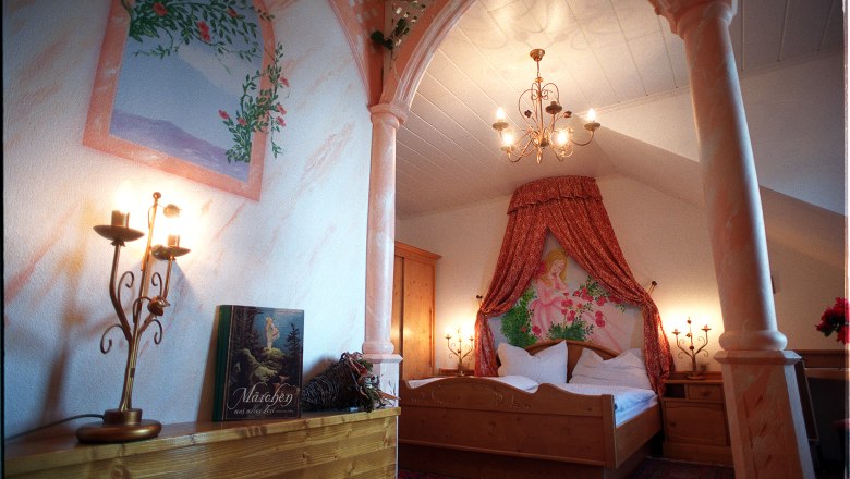 Ein romantisch dekoriertes Schlafzimmer mit Baldachin, Kerzenleuchtern und einem Märchenbuch auf einem Regal.