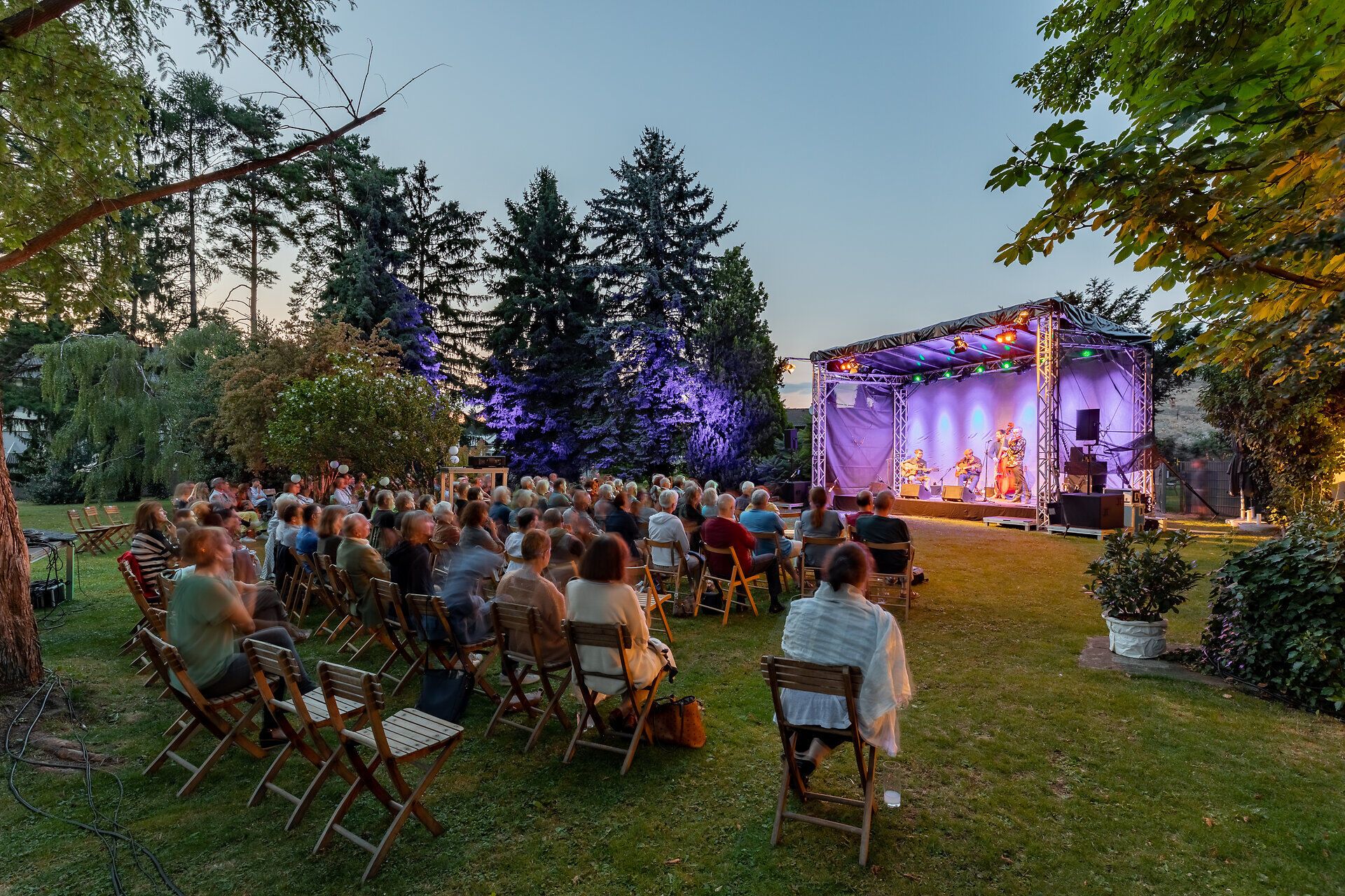 Auf einer Bühne geben vier Musiker ein Open Air Konzert vor Publikum.