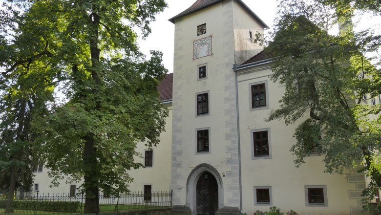 Historisches Geb&auml;ude mit Turm und B&auml;umen im Vordergrund.