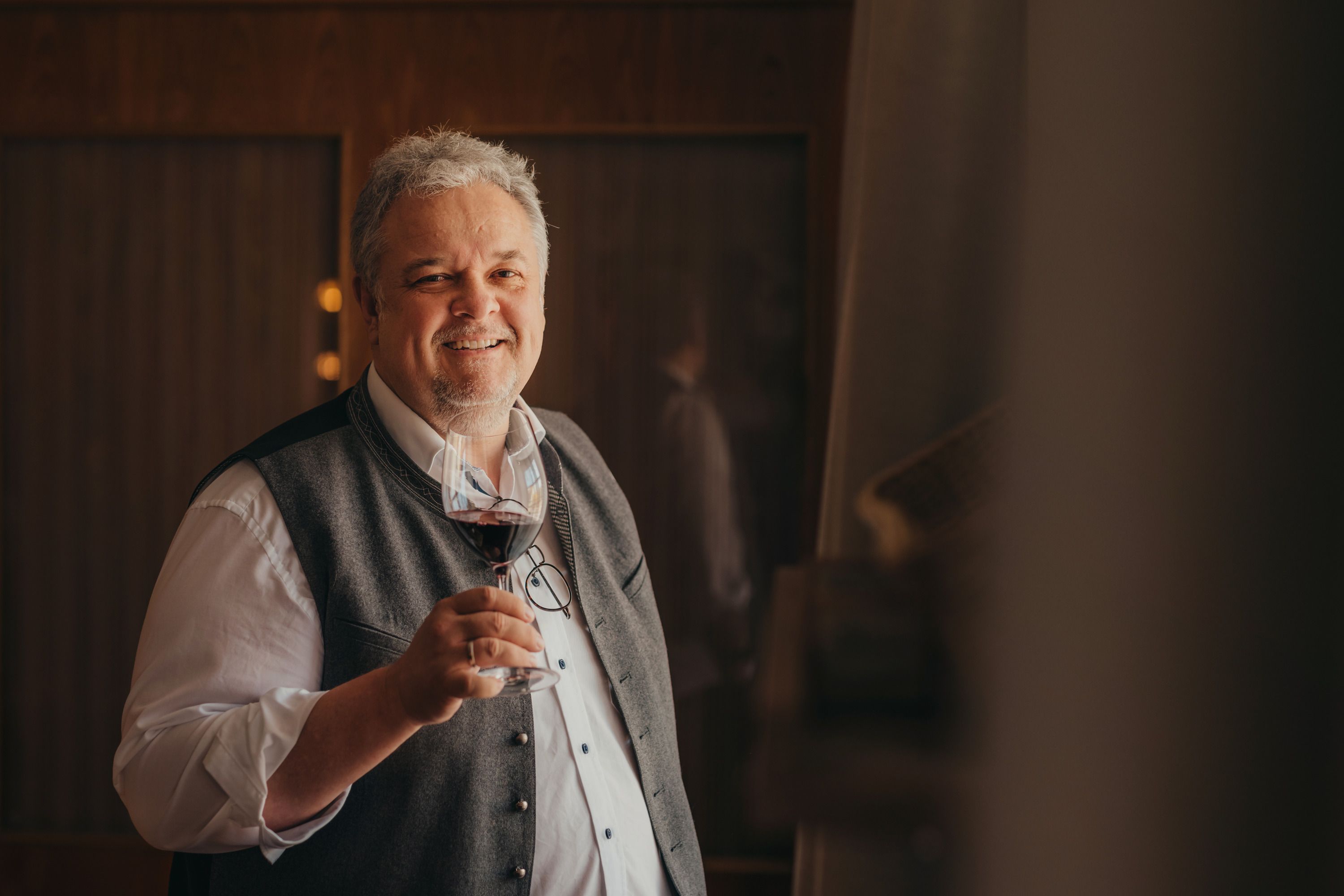 Ein lächelnder Mann in traditioneller Kleidung hält ein Glas Rotwein.