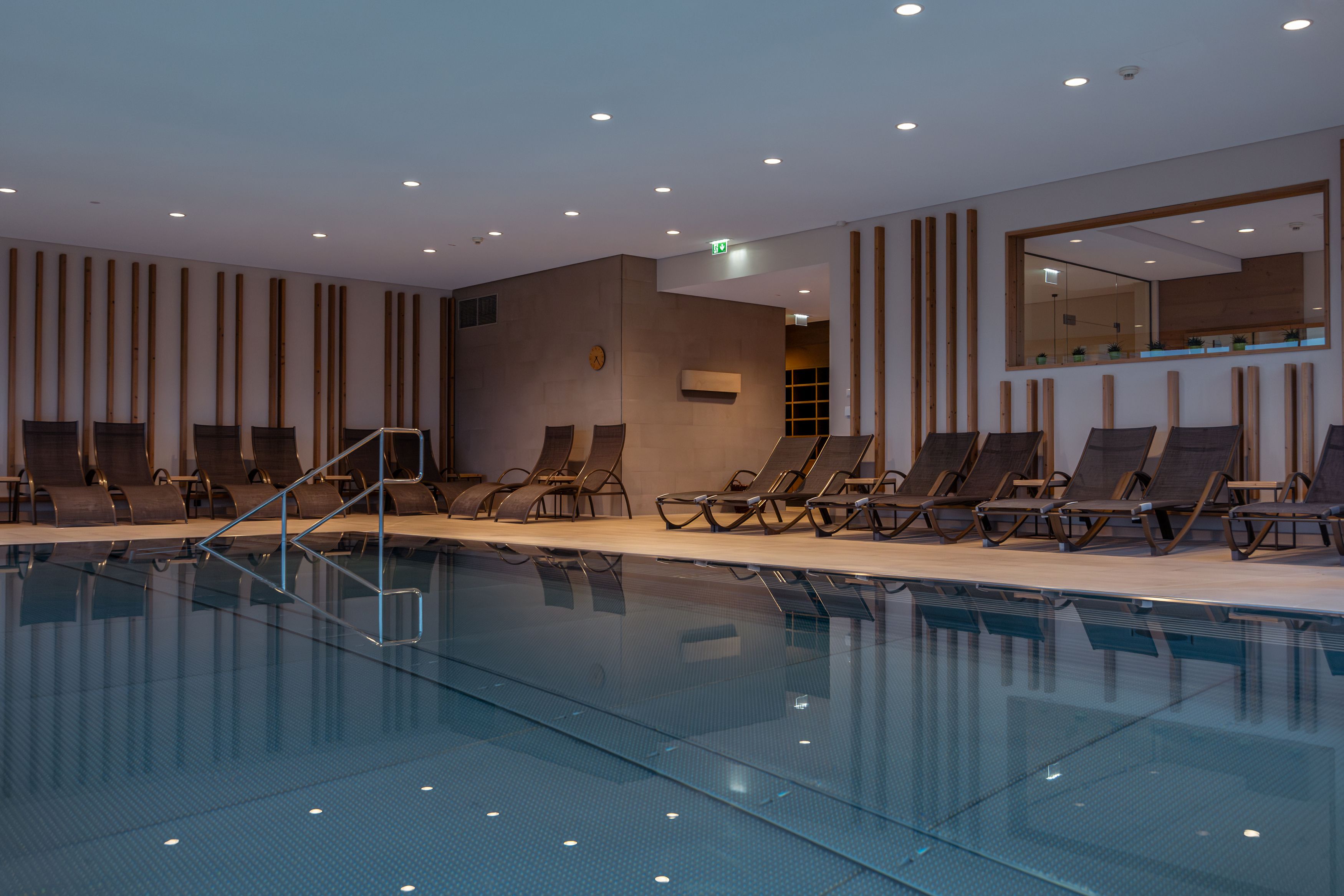 Innenansicht eines Hotelpools mit Liegestühlen und moderner Beleuchtung.