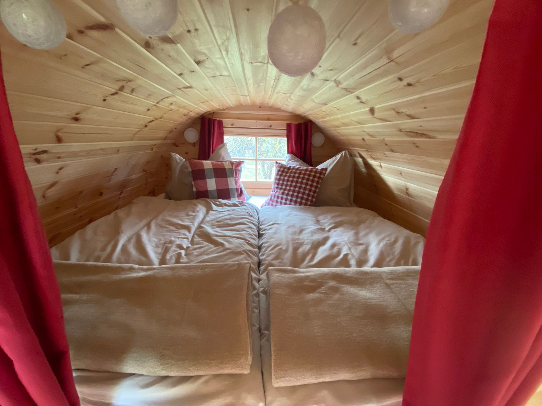 Ein gemütliches Doppelbett in einem Raum mit Holzverkleidung und roten Vorhängen.