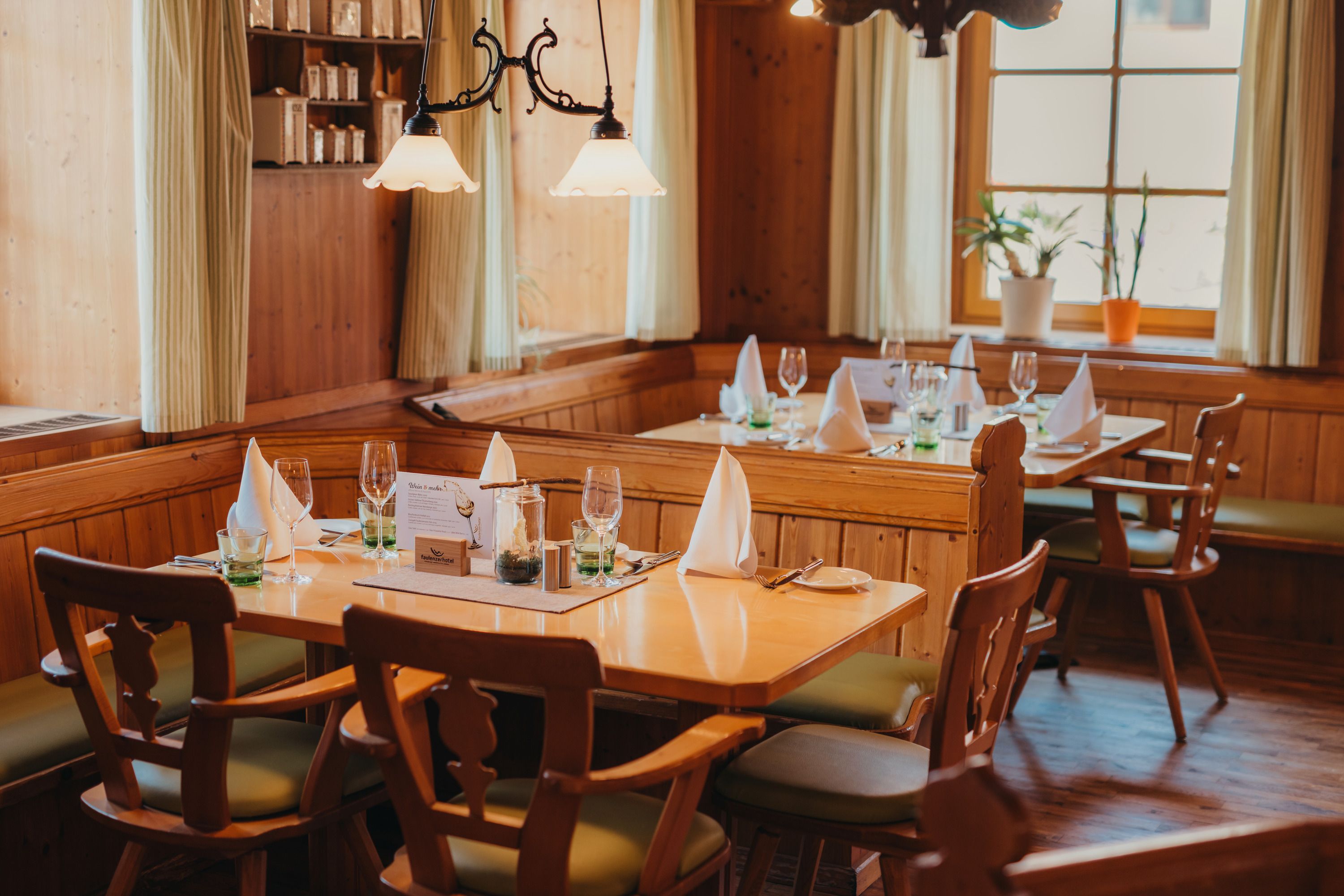 Gemütliches Restaurant mit Holzmöbeln, gedeckten Tischen und Pflanzen am Fenster.