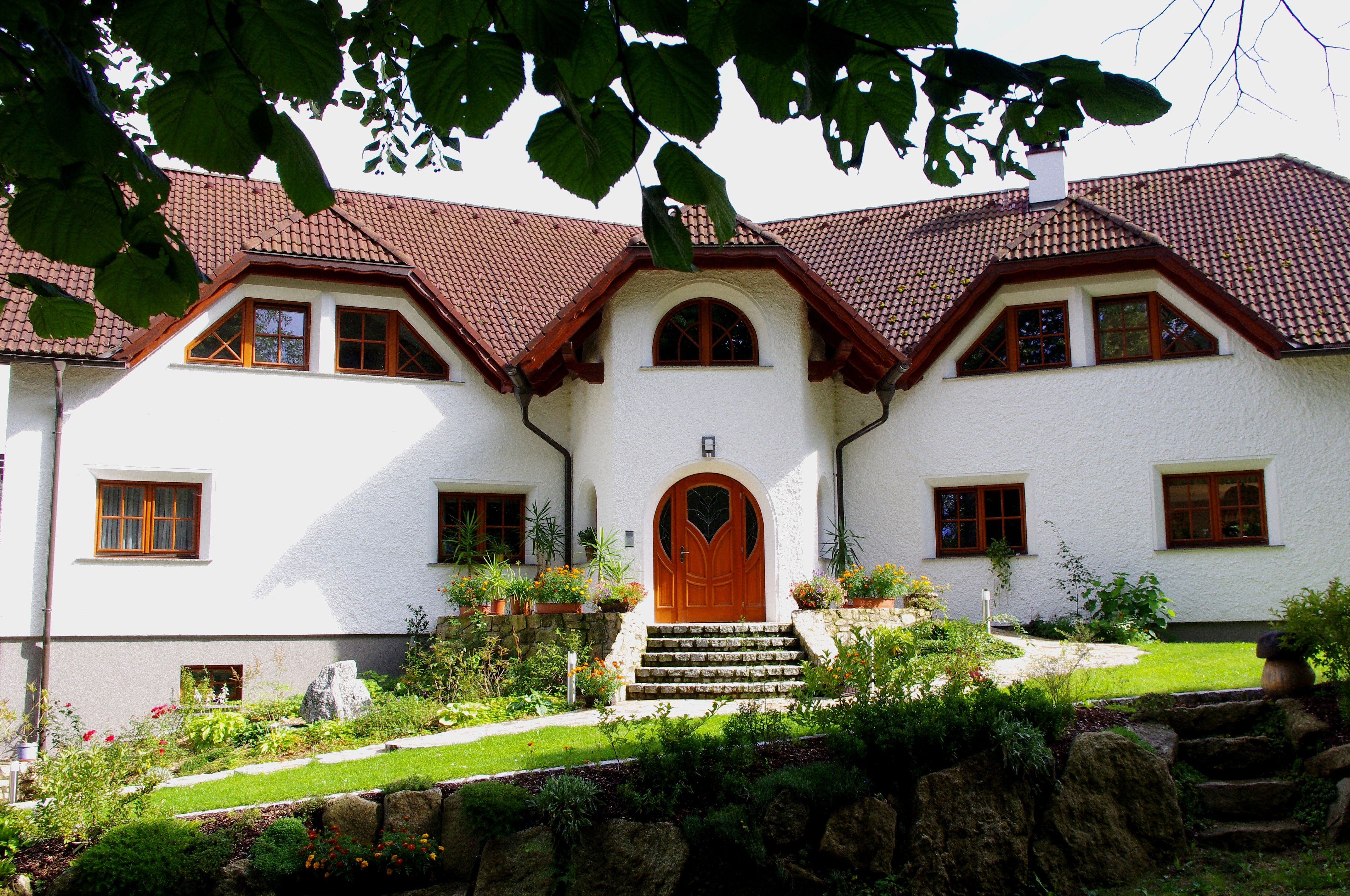 Ein großes, weißes Haus mit rotem Ziegeldach und gepflegtem Garten, umgeben von Bäumen.