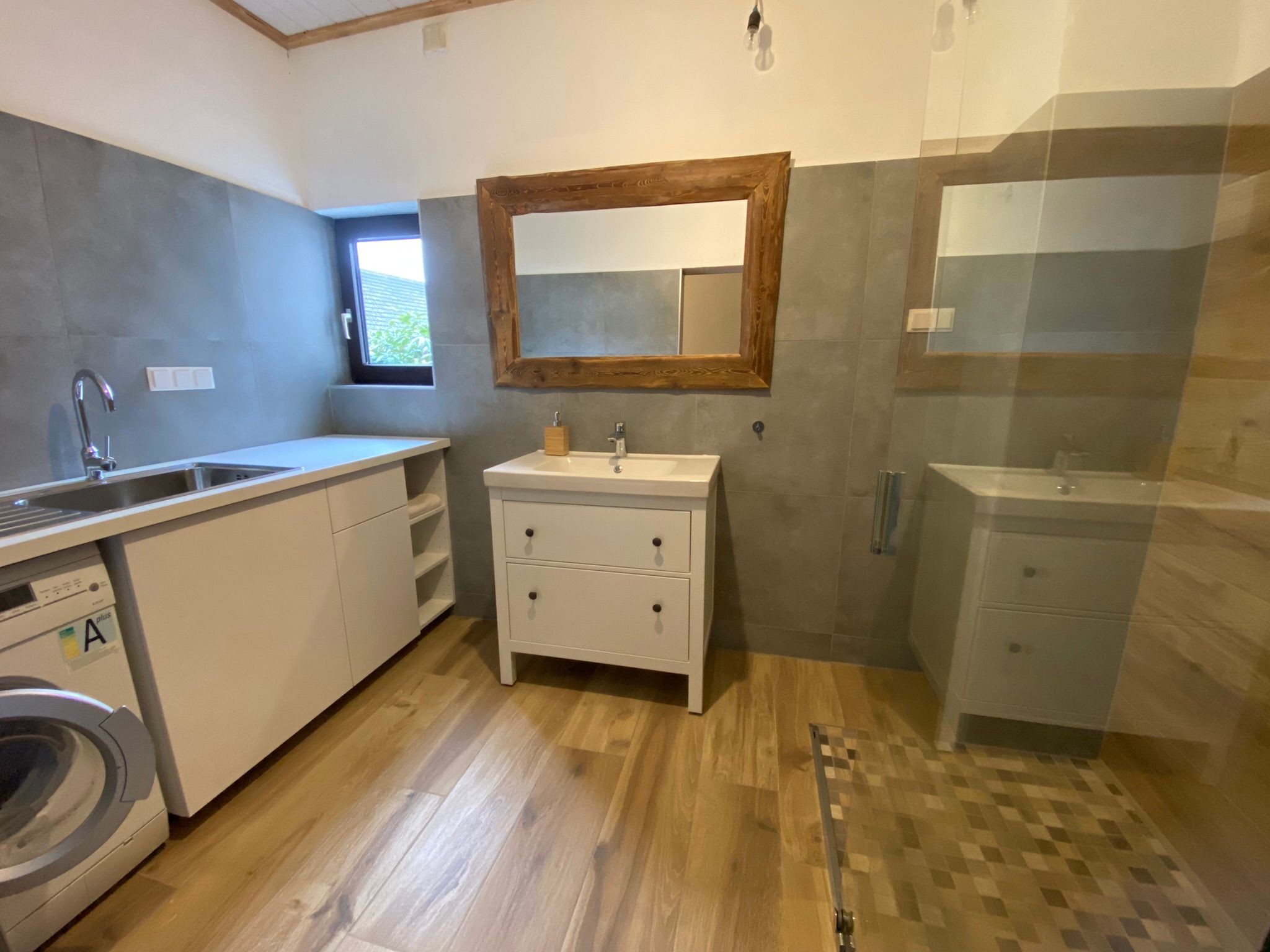 Modernes Badezimmer mit Waschbecken, Spiegel, Waschmaschine und Dusche.
