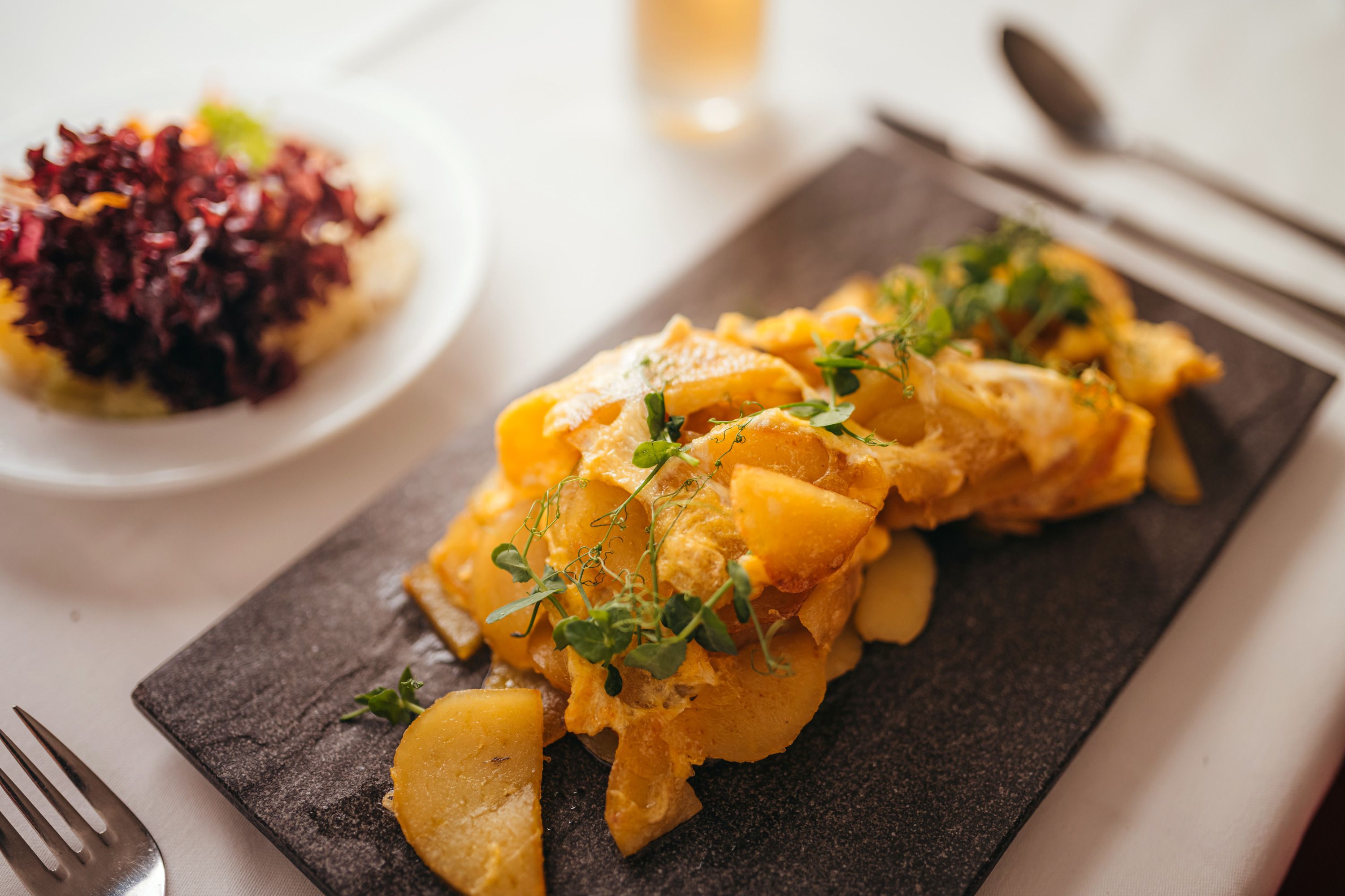 Geröstete Kartoffelscheiben mit Kräutern auf einem schwarzen Teller, daneben ein Salat.