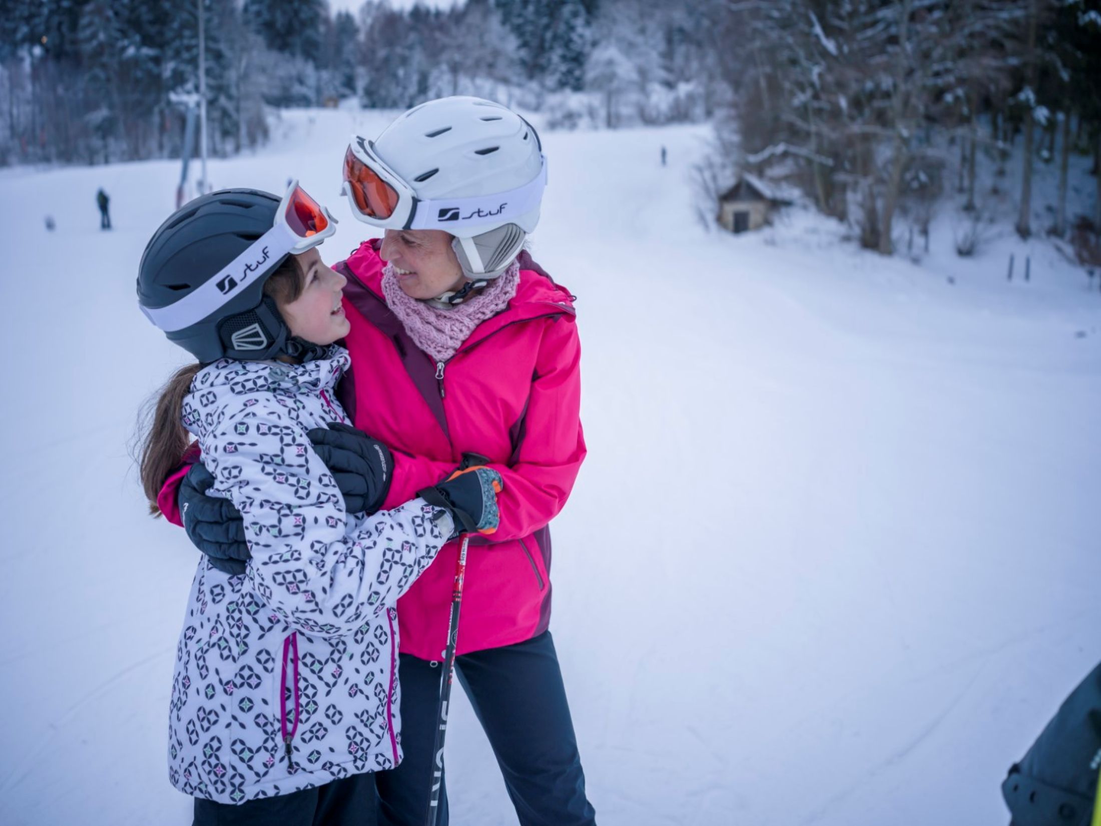 Zwei Personen in Skiausrüstung umarmen sich auf einer Skipiste.