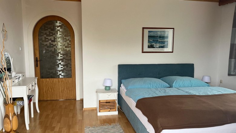 Schlafzimmer mit Doppelbett, Kommode und Holzt&uuml;r.