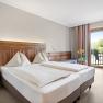 Ein gem&uuml;tliches Hotelzimmer mit Doppelbett, Holzm&ouml;beln und Balkon mit Blick ins Gr&uuml;ne.