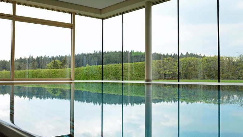 Innenpool mit gro&szlig;en Fenstern und Blick auf Wald und Hecken.