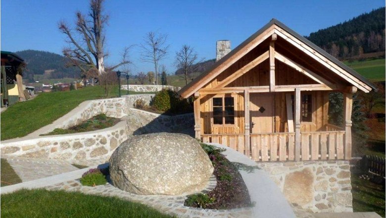 Kleines Holzhaus in einem Garten mit Steinmauern und gro&szlig;em Felsen.