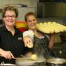 Zwei Frauen in einer K&uuml;che, eine h&auml;lt einen Tablett mit Kn&ouml;deln, die andere kocht Kn&ouml;del in einem Topf.