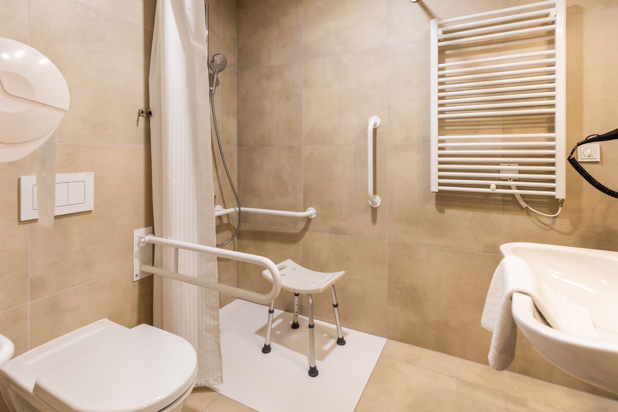 Barrierefreies Badezimmer mit Haltegriffen, Duschstuhl und Handtuchhalter.