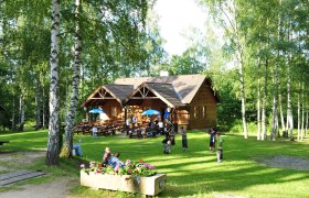 Holzh&uuml;tte im Naturpark Blockheide mit spielenden Kindern und B&auml;umen.