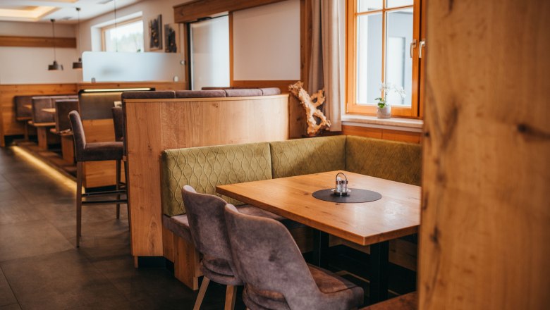 Gem&uuml;tliche Gaststube mit Holzm&ouml;beln und gepolsterten Sitzb&auml;nken, Fenster mit Vorh&auml;ngen, Tisch mit Salz- und Pfefferstreuer.