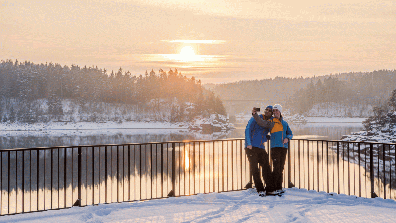 Zwei Personen machen ein Selfie am verschneiten Stausee Ottenstein bei Sonnenuntergang.