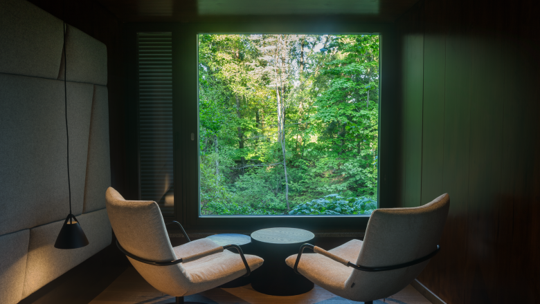 Innenansicht eines modernen Baumhauses mit zwei Sesseln und gro&szlig;em Fenster mit Waldblick.