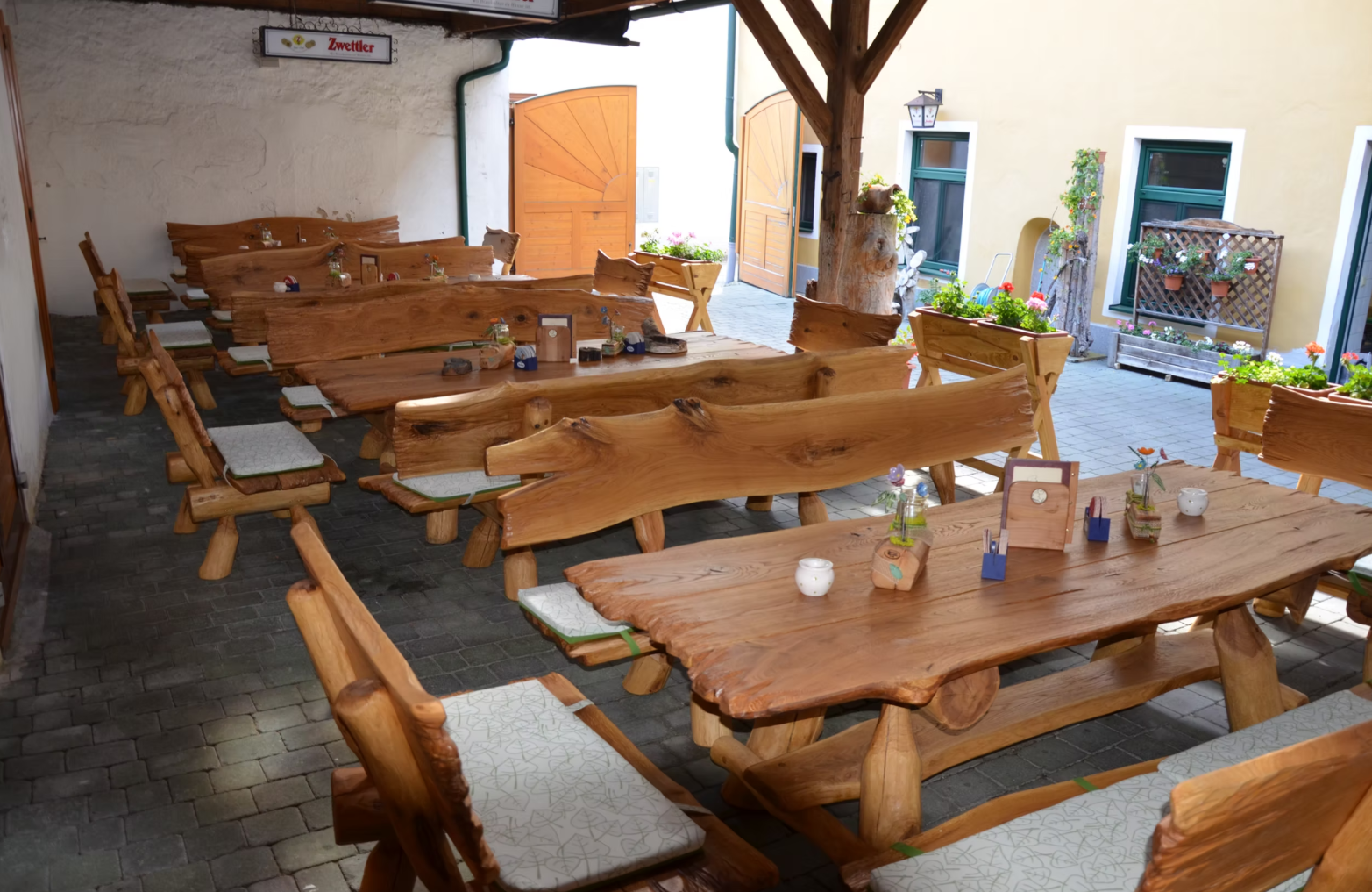 Rustikale Holzbänke und Tische in einem Gasthaus-Innenhof mit Blumen und Dekorationen.