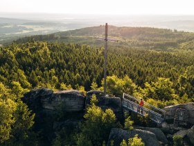Aussichtsplattform auf einer Felsformation mit Blick über dicht bewaldete Hügel im Waldviertel, unter einem klaren blauen Himmel.