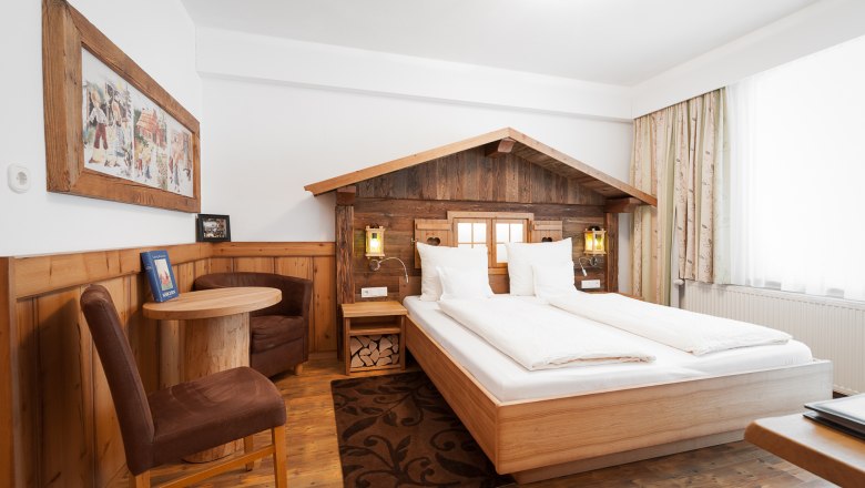 Gem&uuml;tliches Hotelzimmer im Stil von H&auml;nsel und Gretel mit Holzm&ouml;beln und dekorativem Bettkopfteil.