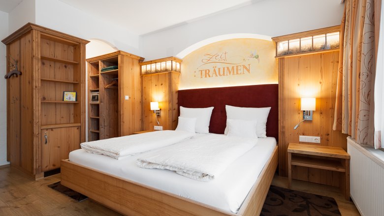 Gem&uuml;tliches Schlafzimmer mit Holzm&ouml;beln, Doppelbett und Schriftzug 'Zeit zum Tr&auml;umen' an der Wand.