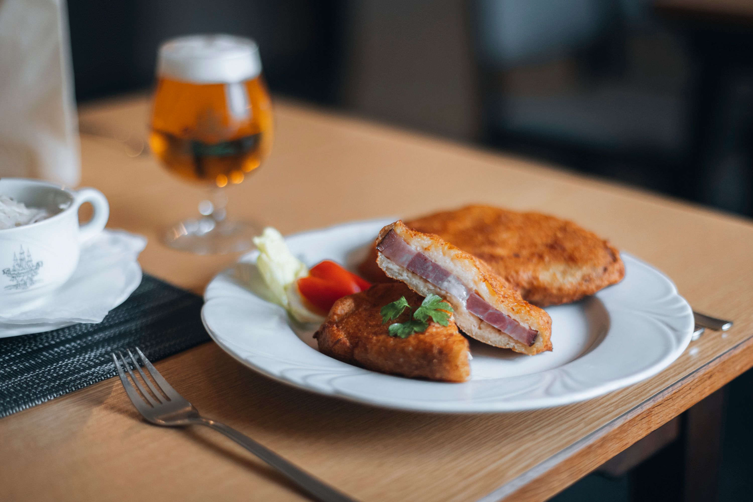 Ein Teller mit Schweinsschopf im Erdäpfelmantel, serviert mit Salat und einem Glas Bier im Hintergrund.
