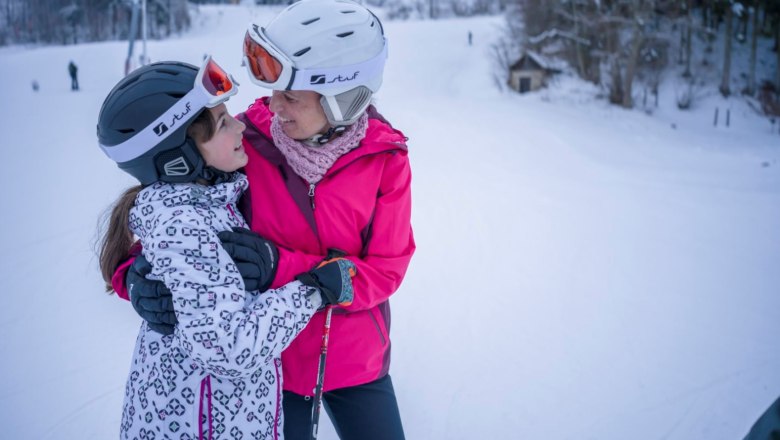Zwei Personen in Skiausr&uuml;stung umarmen sich auf einer Skipiste.
