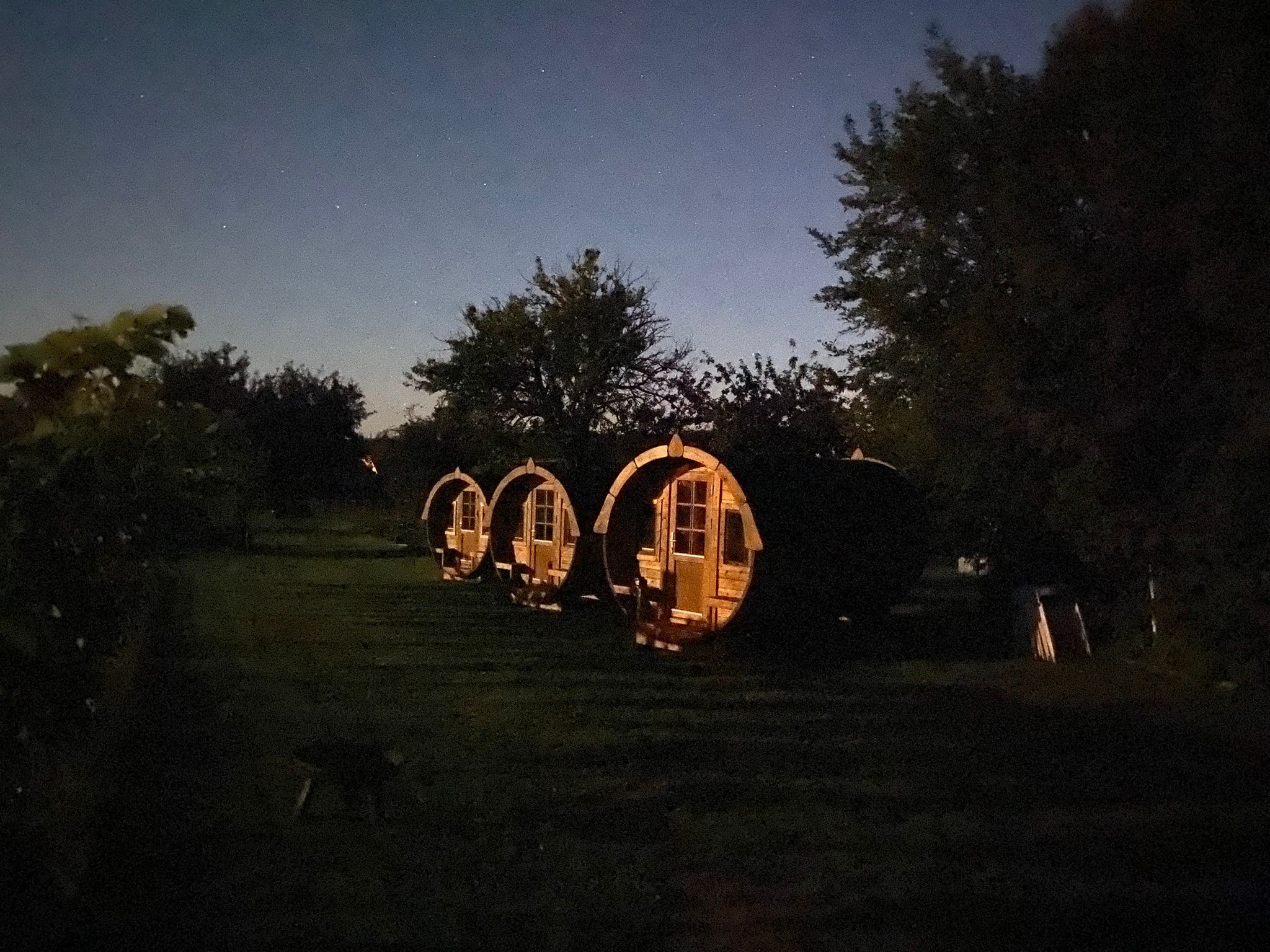 Drei beleuchtete Fasshütten auf einem dunklen Feld bei Nacht.