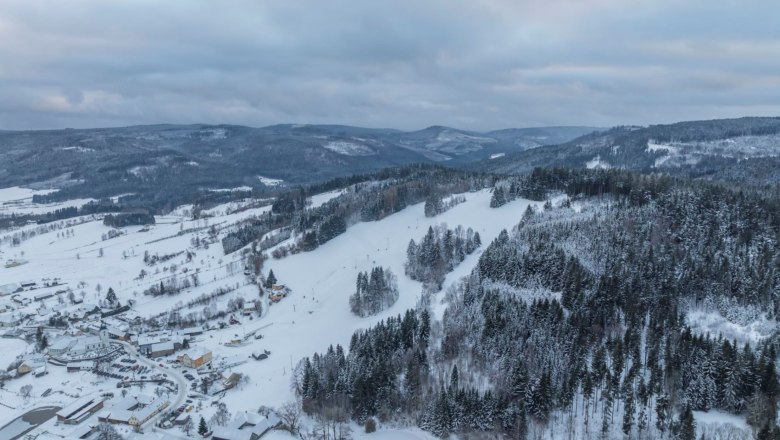 Luftaufnahme einer verschneiten Landschaft mit H&uuml;geln und W&auml;ldern.