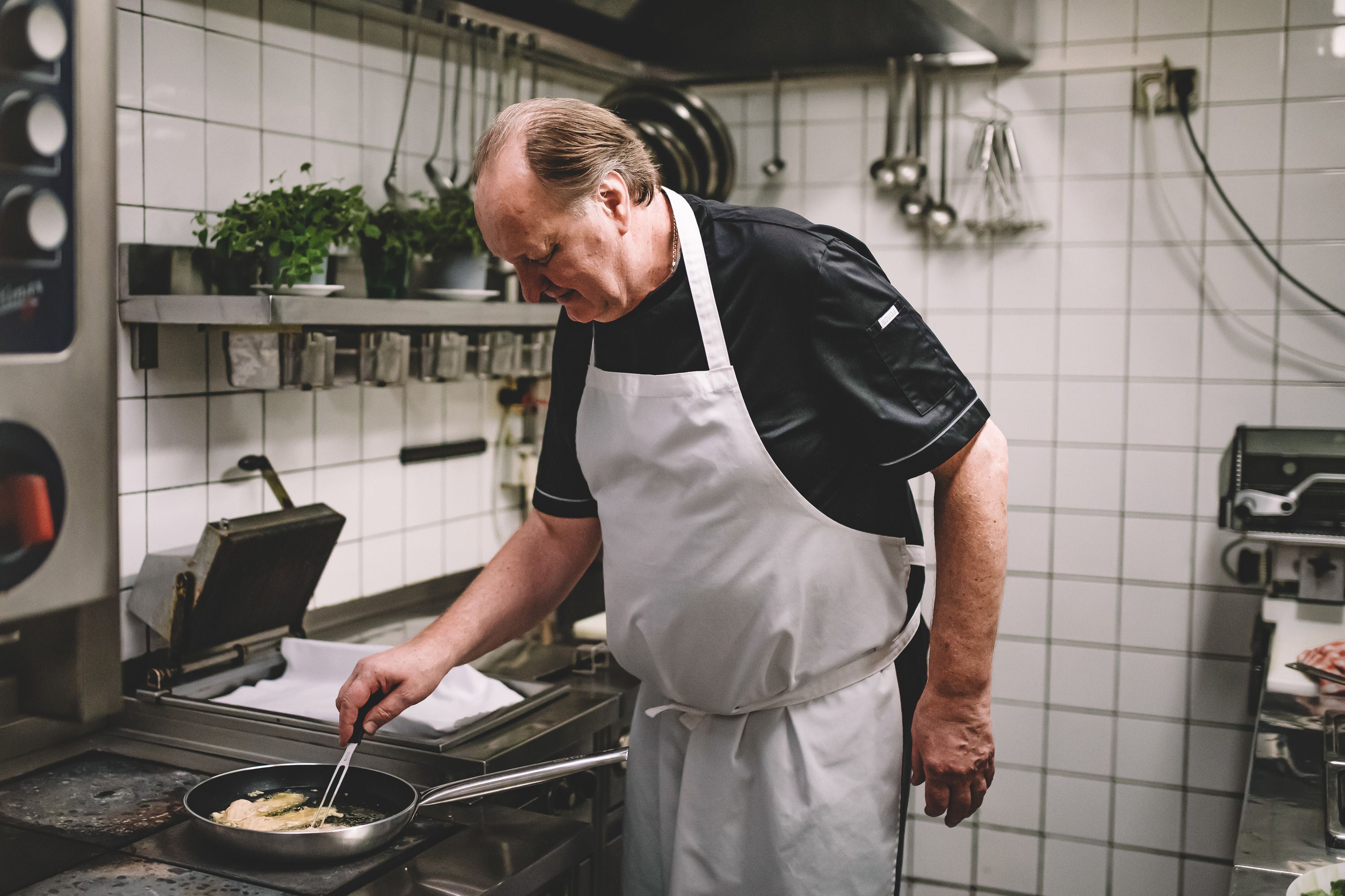 Ein Koch in einer professionellen Küche brät etwas in einer Pfanne.