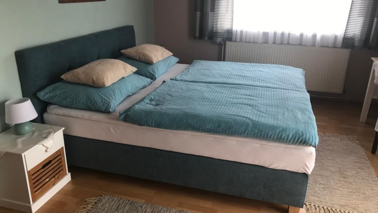 Schlafzimmer mit Doppelbett, blauer Bettw&auml;sche und Nachttisch mit Lampe.