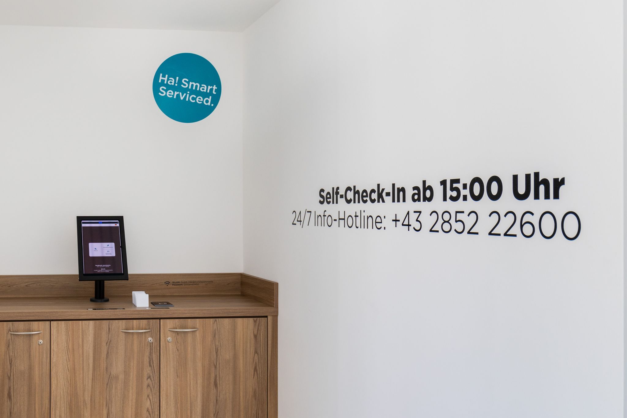 Ein Self-Check-In-Bereich mit einem Bildschirm und einer Telefonnummer für 24/7-Hotline an der Wand.