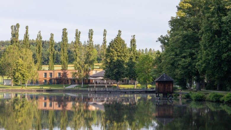 See mit Ufergeb&auml;ude und B&auml;umen, ruhige Landschaftsszene.