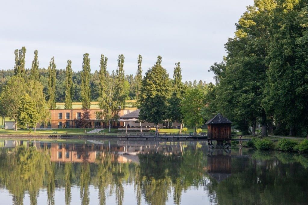 See mit Ufergebäude und Bäumen, ruhige Landschaftsszene.